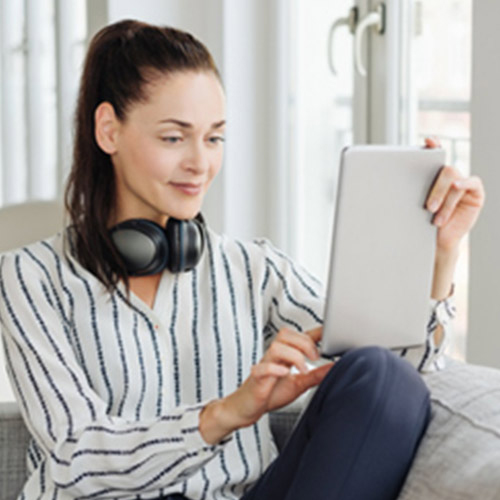 Young woman with long hair and headphones holds a tablet in her hands.